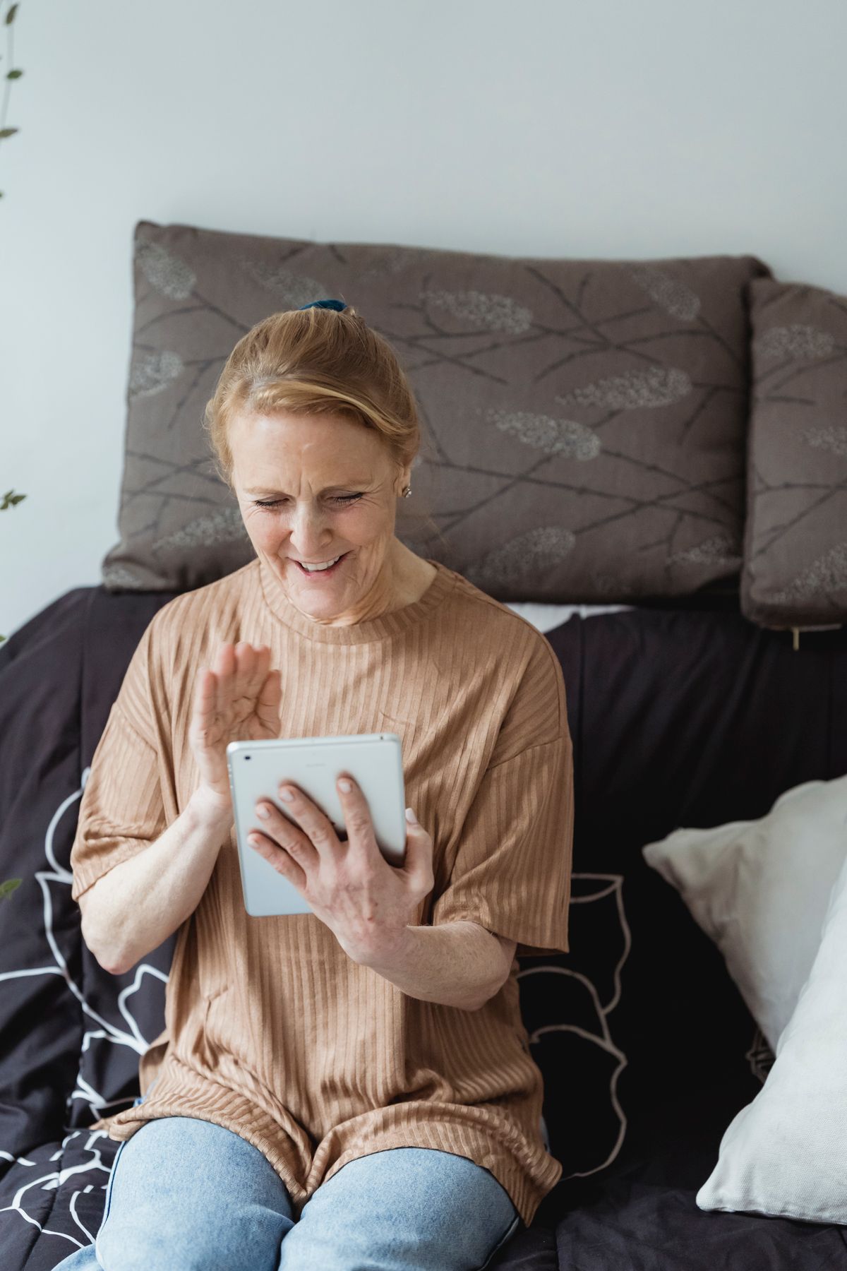 An older woman smiling and waving during a tablet video call at home